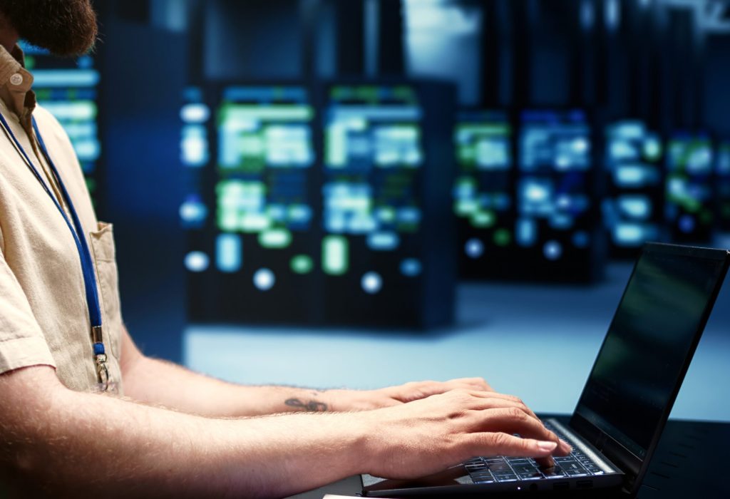 Supervisor running blade servers diagnostic tests and bug checking utilities to determine and repair software issues. Technician using laptop to survey critical systems, checking for flaws, close up